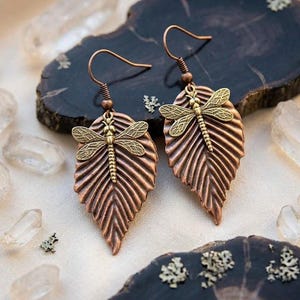 May include: A set of three ceramic mugs with a speckled, matte finish. The mugs are in shades of cream, light brown, and dark brown. Each mug has a simple, minimalist design and a rounded handle. The mugs are likely for coffee or tea.