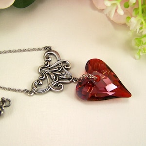 May include: A silver necklace with a delicate filigree design and a dangling red crystal heart pendant.