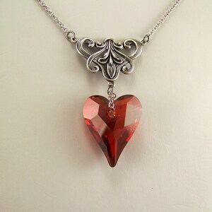 May include: A silver necklace with a delicate filigree design and a dangling red crystal heart pendant.