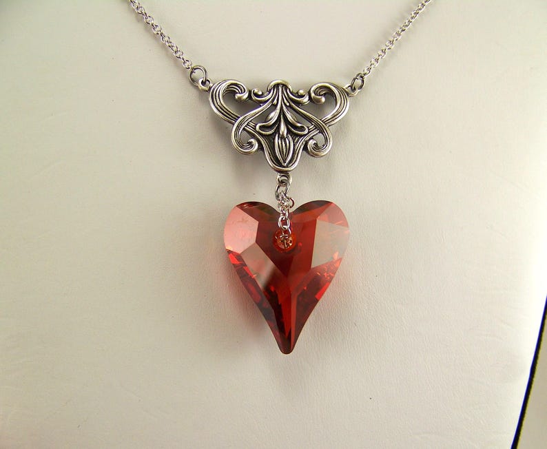 May include: A silver necklace with a delicate filigree design and a dangling red crystal heart pendant.