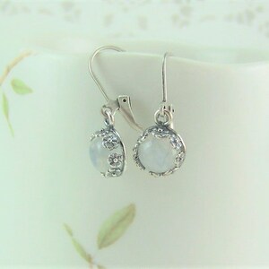 May include: A pair of silver earrings with a white moonstone cabochon set in a floral design.