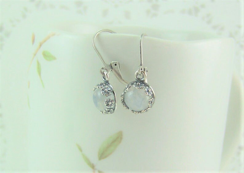 May include: A pair of silver earrings with a white moonstone cabochon set in a floral design.