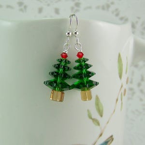 Peut inclure: Une paire de boucles d'oreilles pendantes en argent avec des breloques en cristal vert en forme de sapin de No&euml;l surmont&eacute;es de cristaux rouges.