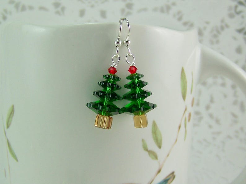 Peut inclure: Une paire de boucles d'oreilles pendantes en argent avec des breloques en cristal vert en forme de sapin de No&euml;l surmont&eacute;es de cristaux rouges.