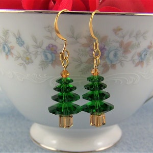 Peut inclure: Une paire de boucles d'oreilles pendantes dor&eacute;es avec des breloques en cristal vert en forme de sapin de No&euml;l. Les sapins sont faits de cristaux verts facet&eacute;s et ont une perle dor&eacute;e au bas.