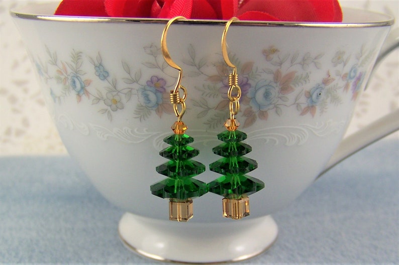 Peut inclure: Une paire de boucles d'oreilles pendantes dor&eacute;es avec des breloques en cristal vert en forme de sapin de No&euml;l. Les sapins sont faits de cristaux verts facet&eacute;s et ont une perle dor&eacute;e au bas.