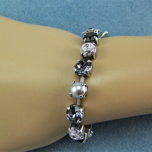 Puede incluir: Una pulsera que presenta una serie de piedras redondas engastadas en tonos variados de negro, gris y plata. El dise&ntilde;o incluye cristales oscuros facetados, una cuenta gris lisa similar a una perla y piedras transparentes en un marco plateado.