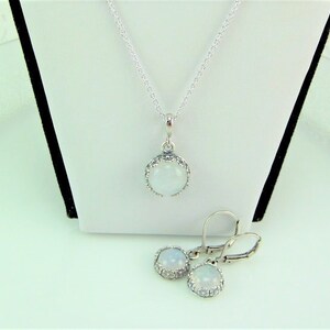 May include: A silver necklace and earrings set with a white moonstone pendant and matching earrings. The pendant and earrings are set in a silver halo.