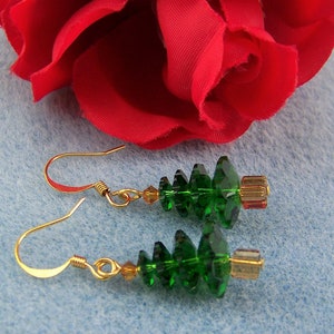 Peut inclure: Une paire de boucles d'oreilles en forme de sapin de No&euml;l en cristal vert avec des crochets dor&eacute;s. Les boucles d'oreilles sont pendantes et pr&eacute;sentent un design &agrave; plusieurs niveaux.