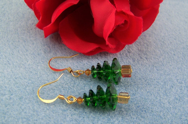 Peut inclure: Une paire de boucles d'oreilles en forme de sapin de No&euml;l en cristal vert avec des crochets dor&eacute;s. Les boucles d'oreilles sont pendantes et pr&eacute;sentent un design &agrave; plusieurs niveaux.