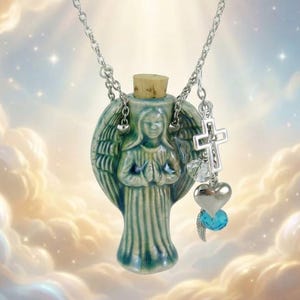May include: A ceramic angel pendant necklace with a silver chain. The angel-shaped pendant is teal and has a cork stopper. Additional charms include a silver cross, a heart, and a blue crystal. The background features a cloudy sky.