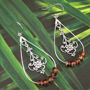 May include: Silver teardrop earrings with a floral design and brown glass beads.