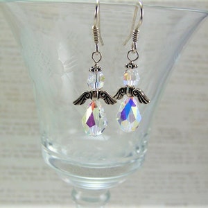 Puede incluir: Un par de pendientes con forma de &aacute;ngel. Cada pendiente presenta un cuerpo de cristal transparente e iridiscente en forma de l&aacute;grima, alas plateadas y una cabeza de cristal transparente. Los pendientes cuelgan de alambres plateados.