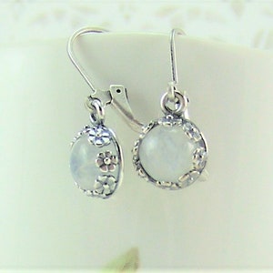May include: A pair of silver earrings with a white moonstone cabochon set in a floral design.