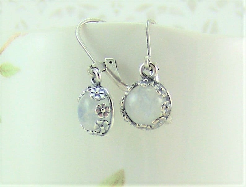 May include: A pair of silver earrings with a white moonstone cabochon set in a floral design.