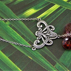 May include: A silver chain necklace with a silver filigree pendant and a dangling heart-shaped crystal. The crystal is a deep burgundy color.