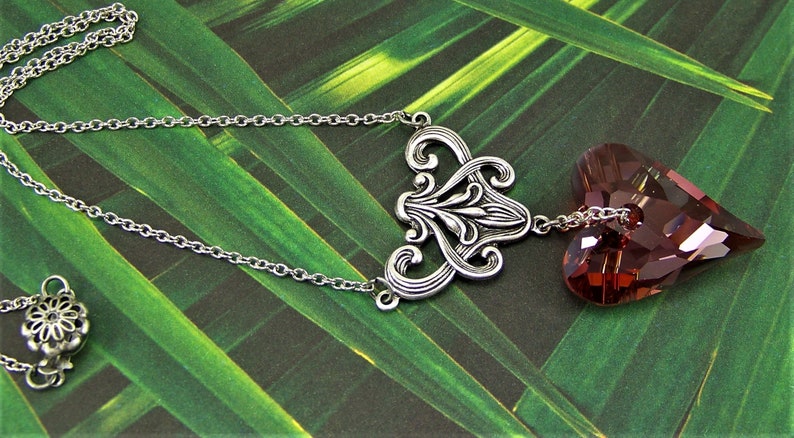 May include: A silver chain necklace with a silver filigree pendant and a dangling heart-shaped crystal. The crystal is a deep burgundy color.