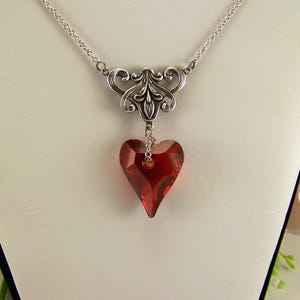 May include: A silver chain necklace with a silver filigree pendant and a red crystal heart.