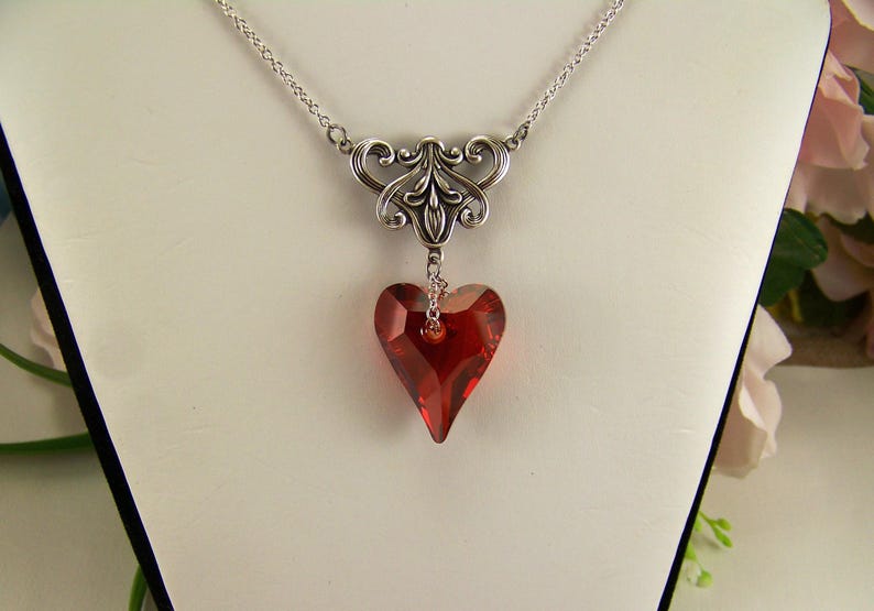 May include: A silver chain necklace with a silver filigree pendant and a red crystal heart.