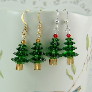 May include: Three pairs of Christmas tree earrings. Each earring features a green crystal tree with a red crystal star on top. The trees are suspended from gold and silver hooks.