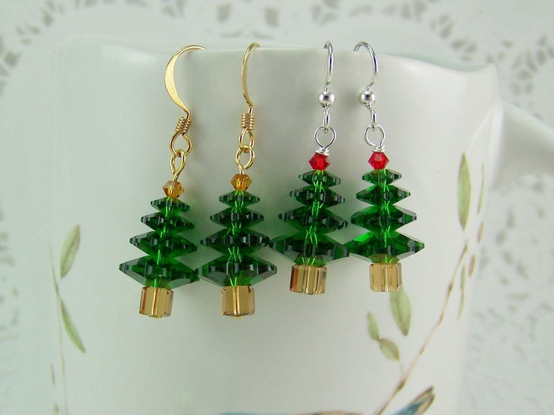Peut inclure: Trois paires de boucles d'oreilles en forme de sapin de No&euml;l. Chaque boucle d'oreille pr&eacute;sente un sapin en cristal vert avec une &eacute;toile en cristal rouge au sommet. Les sapins sont suspendus &agrave; des crochets dor&eacute;s et argent&eacute;s.