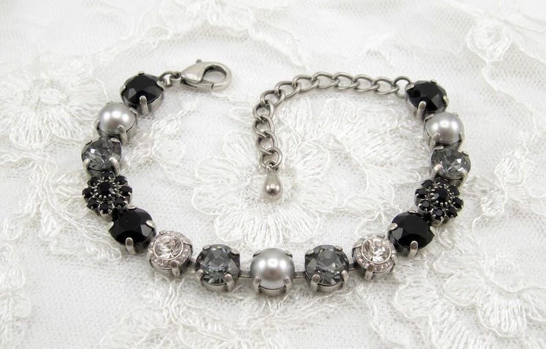 Puede incluir: Una pulsera de tono plateado que presenta una secuencia de cristales facetados en negro, gris y transparente, intercalados con perlas grises lisas. Incluye un cierre de mosquet&oacute;n y una cadena de extensi&oacute;n ajustable con un peque&ntilde;o dije.