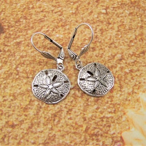 May include: Silver dangle earrings with a sand dollar design. The sand dollars have a textured surface and a five-pointed star in the center.