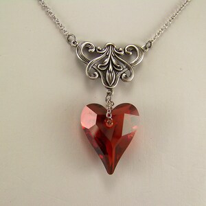 May include: A silver necklace with a delicate filigree design and a dangling red heart-shaped crystal.