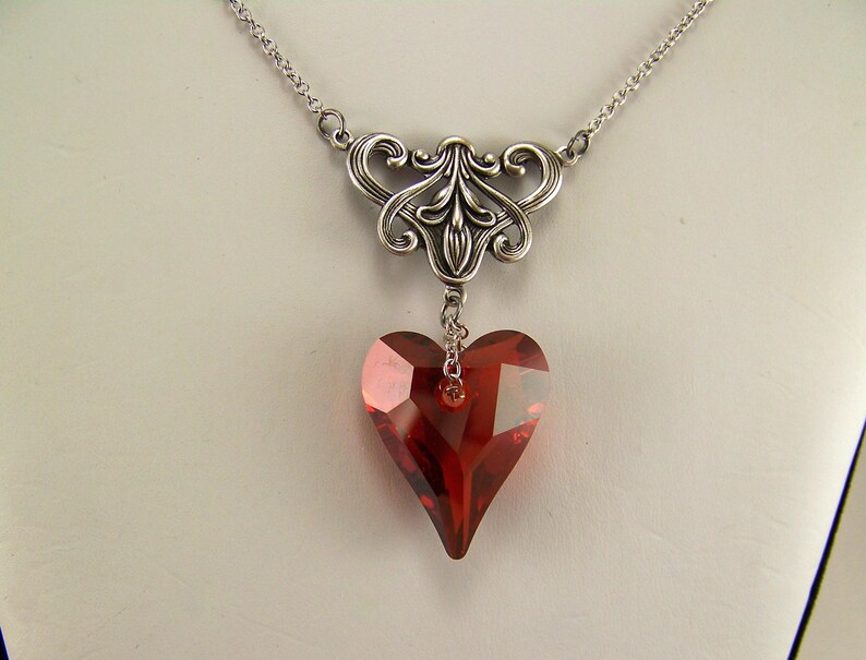 May include: A silver necklace with a delicate filigree design and a dangling red heart-shaped crystal.
