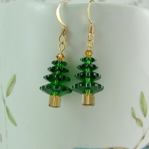 Peut inclure: Une paire de boucles d'oreilles pendantes dor&eacute;es avec des breloques en cristal vert en forme de sapin de No&euml;l. Les sapins sont faits de perles de cristal facett&eacute;es et ont une perle dor&eacute;e au bas.