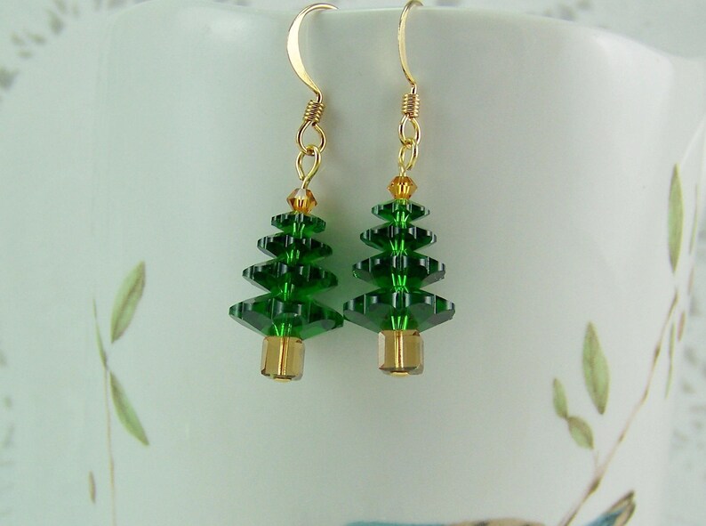 Peut inclure: Une paire de boucles d'oreilles pendantes dor&eacute;es avec des breloques en cristal vert en forme de sapin de No&euml;l. Les sapins sont faits de perles de cristal facett&eacute;es et ont une perle dor&eacute;e au bas.