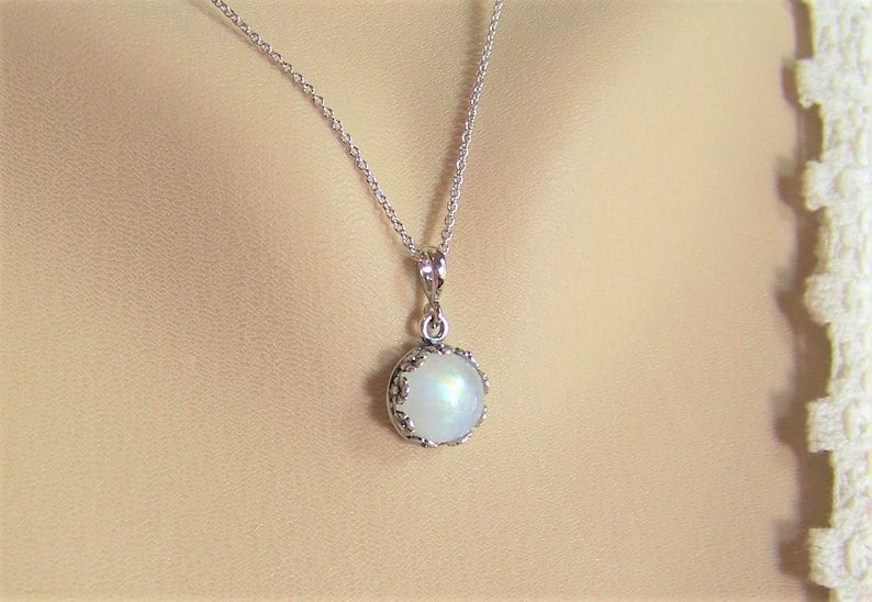 May include: A silver chain necklace with a round, white moonstone pendant set in a silver bezel.