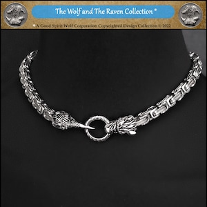 May include: A silver chain necklace with wolf head clasps. The chain is a box chain style. The wolf heads are detailed and have sharp teeth. The necklace is part of the "The Wolf and The Raven Collection" by Good Spirit Wolf Corporation.
