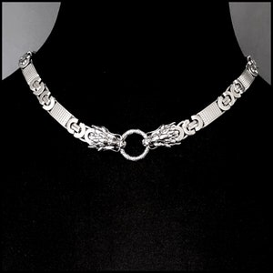 May include: A silver necklace with a dragon head design on each end and a circular ring in the center.