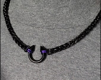 May include: A black chain necklace with a U-shaped pendant. The pendant has two black spikes with purple accents. The necklace is displayed on a gray background.