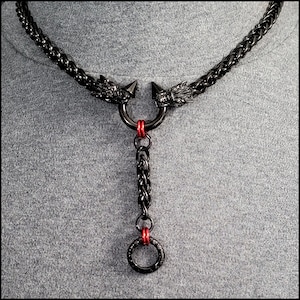 May include: Black metal necklace with a dragon head design and a dangling ring. The necklace has red accents.
