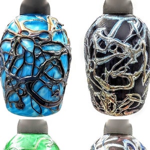 K&ouml;nnte beinhalten: Vier Glasflaschen mit einem einzigartigen, komplizierten Design. Jede Flasche hat eine andere Grundfarbe mit einem silbernen, metallischen, netzartigen Muster.