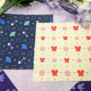 May include: Two microfiber cleaning cloths with different patterns. One cloth is navy blue with yellow and white geometric patterns of fish, fans, and waves. The other cloth is white with yellow and pink geometric patterns of butterflies and flowers.