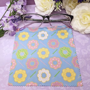 May include: A blue microfiber cleaning cloth with a donut pattern. The cloth is decorated with pink, yellow, and green donuts on a light blue background.