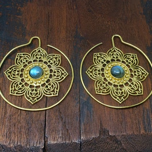 May include: A pair of gold hoop earrings with a delicate, intricate floral design and a blue gemstone in the center of each flower.