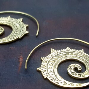 May include: A pair of gold-toned hoop earrings with a spiral design. The earrings are made of metal and have a delicate, intricate pattern.