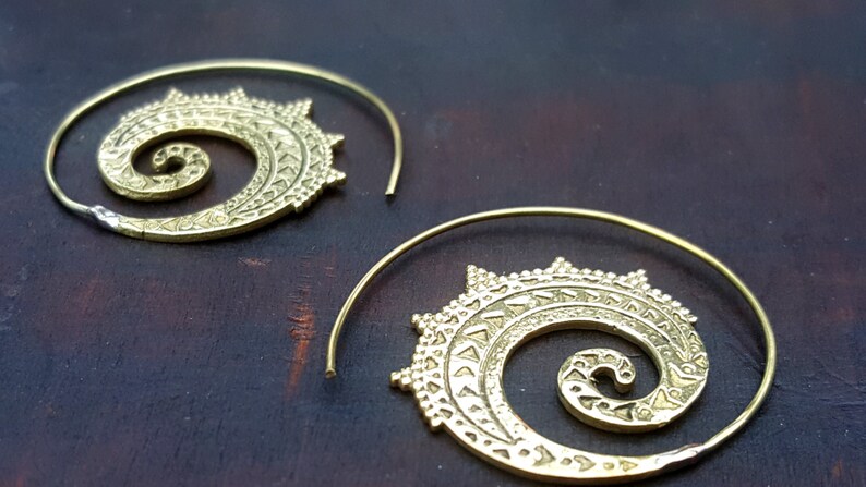 May include: A pair of gold-toned hoop earrings with a spiral design. The earrings are made of metal and have a delicate, intricate pattern.