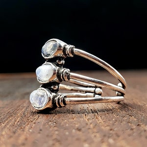 May include: Silver ring featuring three moonstone gems set in a delicate, layered band.