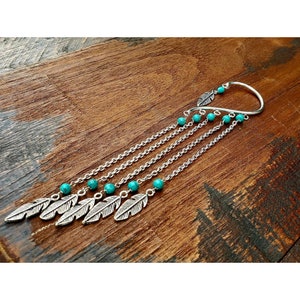 Könnte beinhalten: Silberner Ohrclip mit gebogenem Design und einer herabhängenden Kette mit türkisfarbenen Perlen und silbernen Federschmuck.