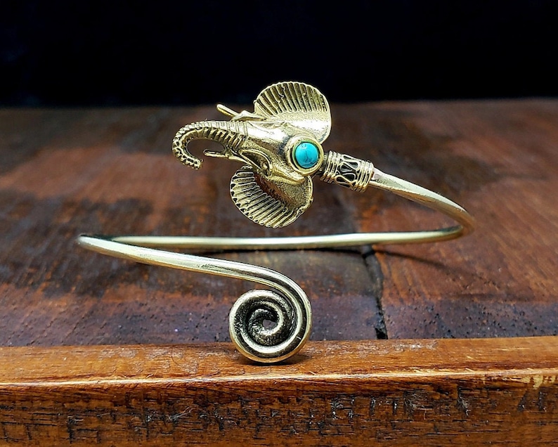 May include: A gold-toned cuff bracelet with an elephant head and a turquoise stone. The bracelet has a spiral design at one end and a detailed elephant head with large ears and a trunk.