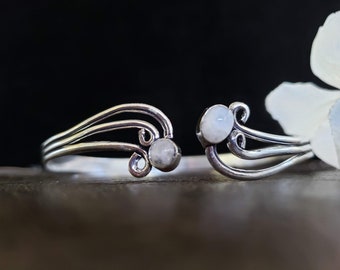 May include: A silver bracelet with two white moonstone accents. The bracelet has a delicate, flowing design.
