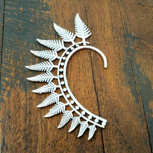 May include: Silver ear cuff with a fern leaf design. The cuff is open and has a curved shape.
