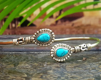May include: A gold bangle bracelet with two turquoise teardrop-shaped stones set in ornate silver settings.