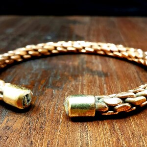 May include: A gold-toned metal bracelet with a woven design. The bracelet is open and has two round, solid metal ends.