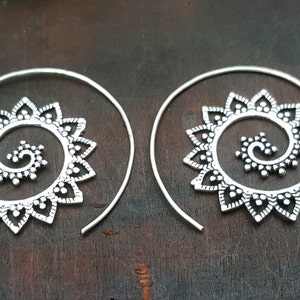 May include: A pair of silver spiral earrings with a delicate floral design. The earrings are made of metal and have a hoop shape.